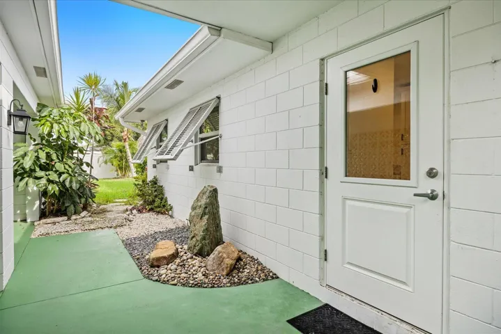 White painted block exterior with green-finished concrete pathway, a decorative rock garden, and louvered windows