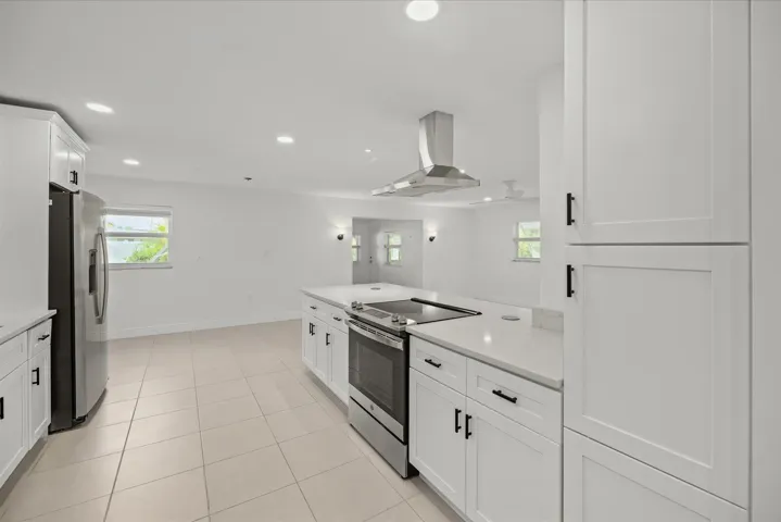 Kitchen featuring white cabinetry, light-toned tile flooring, stainless steel appliances, a center island with integrated cooktop, and recessed lighting