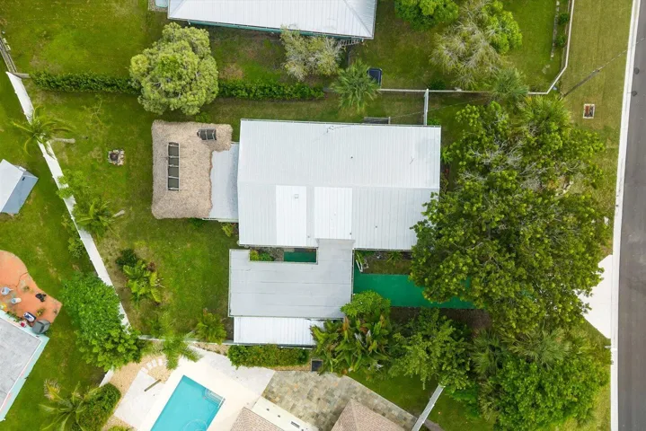 Metal roof structure, adjacent thatch-roofed structure with skylights, expansive green space, mature trees, and a visible swimming pool