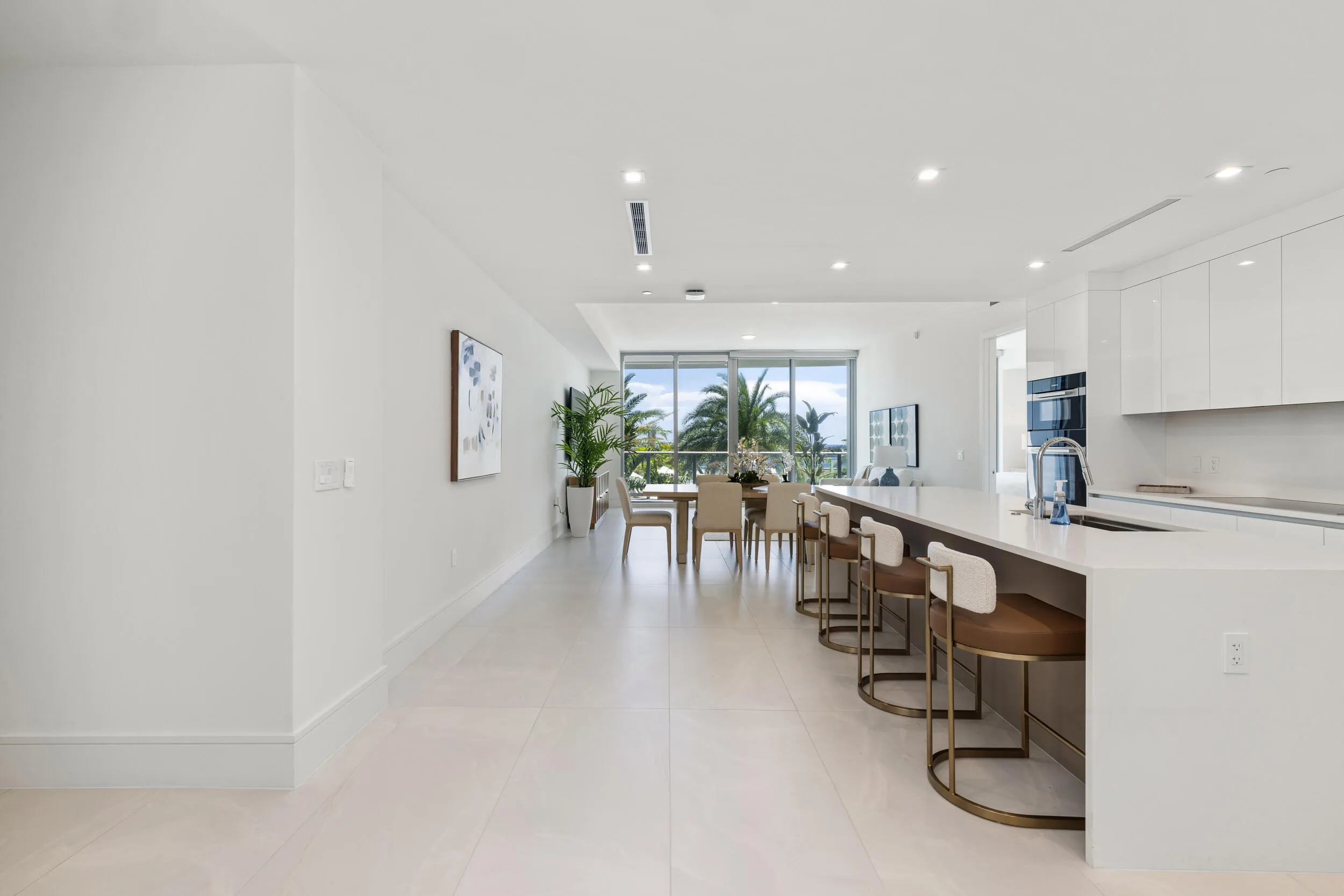 Contemporary open concept living area with light-toned flooring, recessed lighting, expansive floor-to-ceiling windows, and a kitchen island with integrated seating