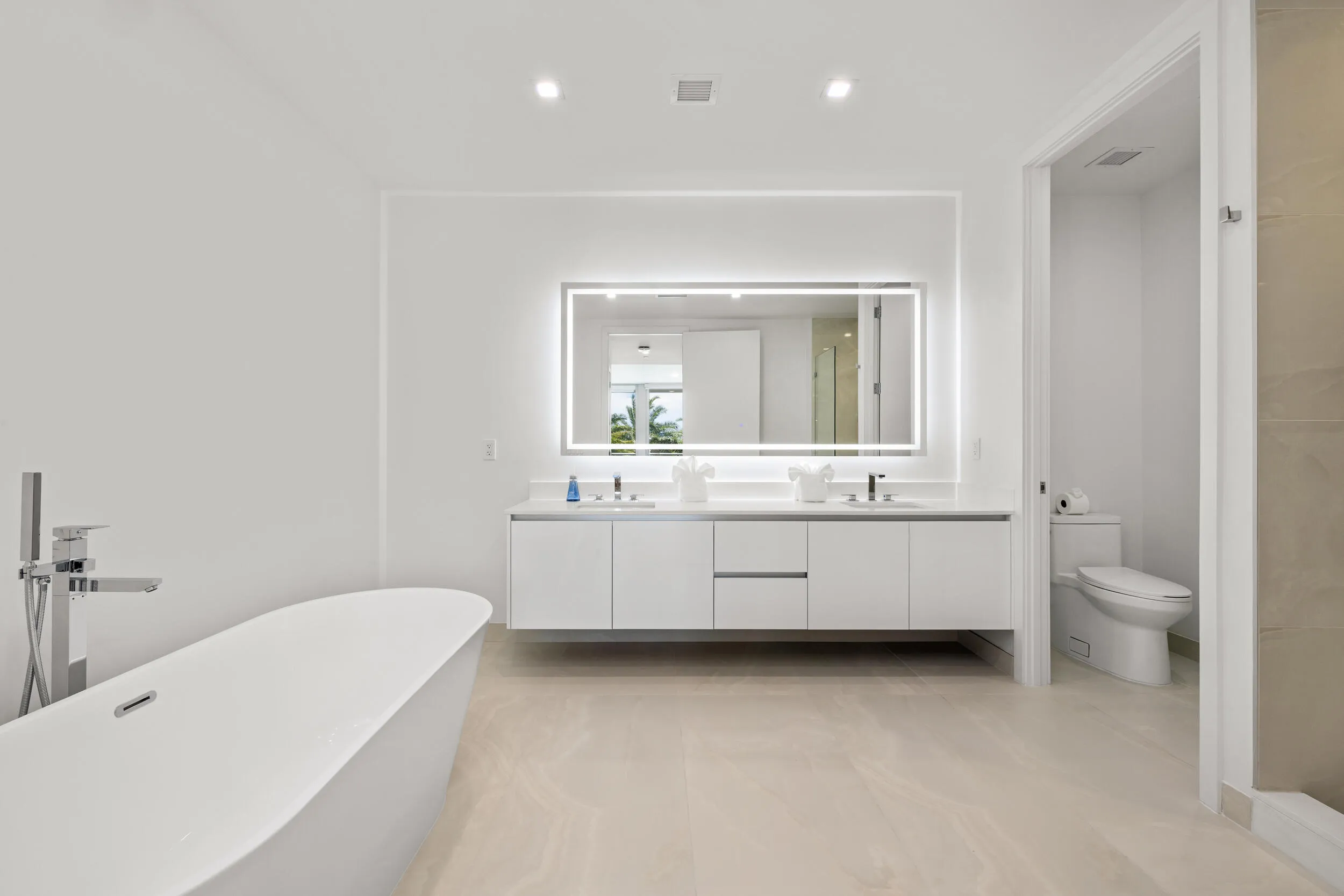 Master Bath - Freestanding soaking tub with floor-mounted chrome faucet, dual vanity with undermount sinks, illuminated mirror, recessed lighting, and large format floor tile
