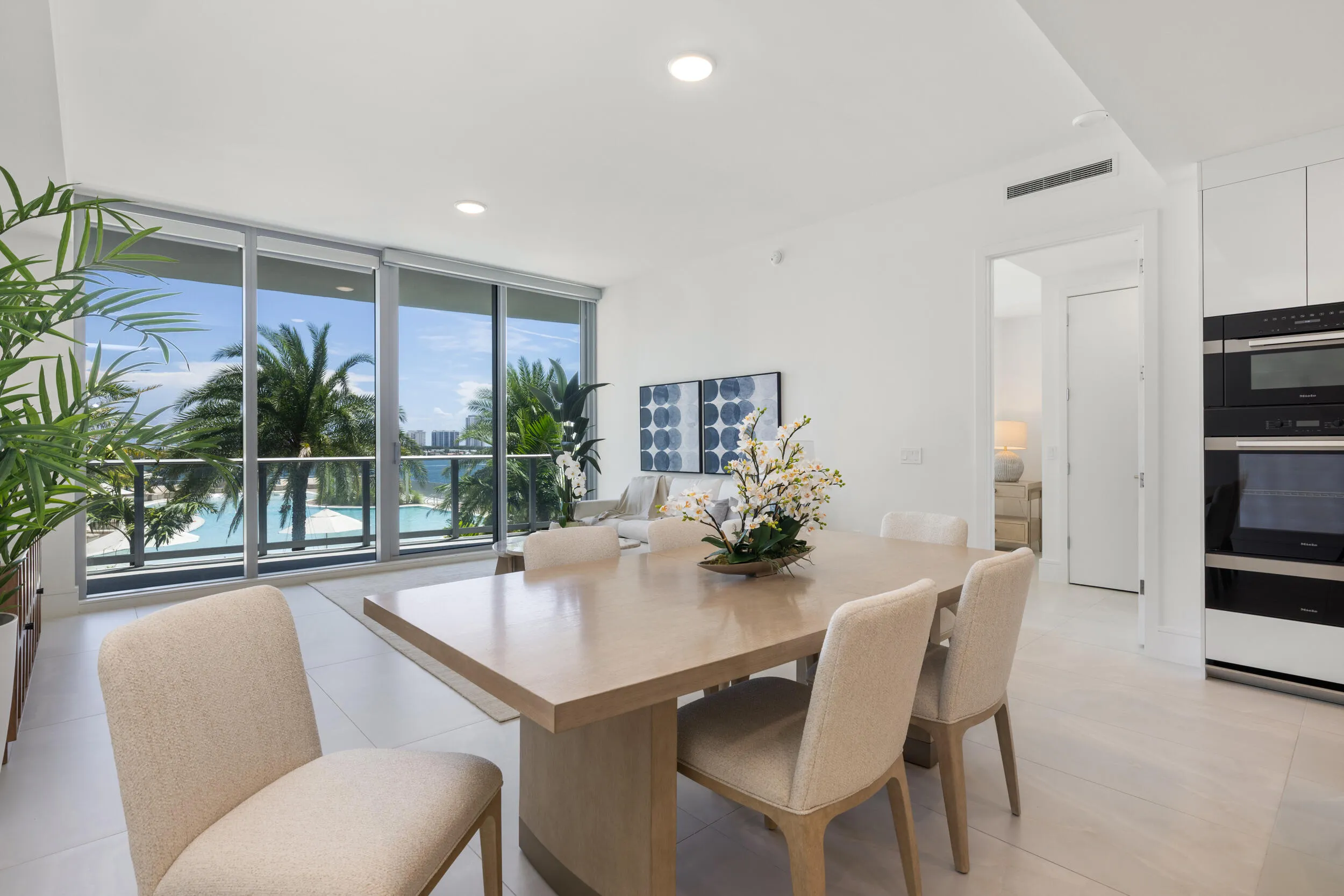 Floor-to-ceiling windows, recessed lighting, white cabinetry with integrated appliances, wood-finish dining table, and tile flooring