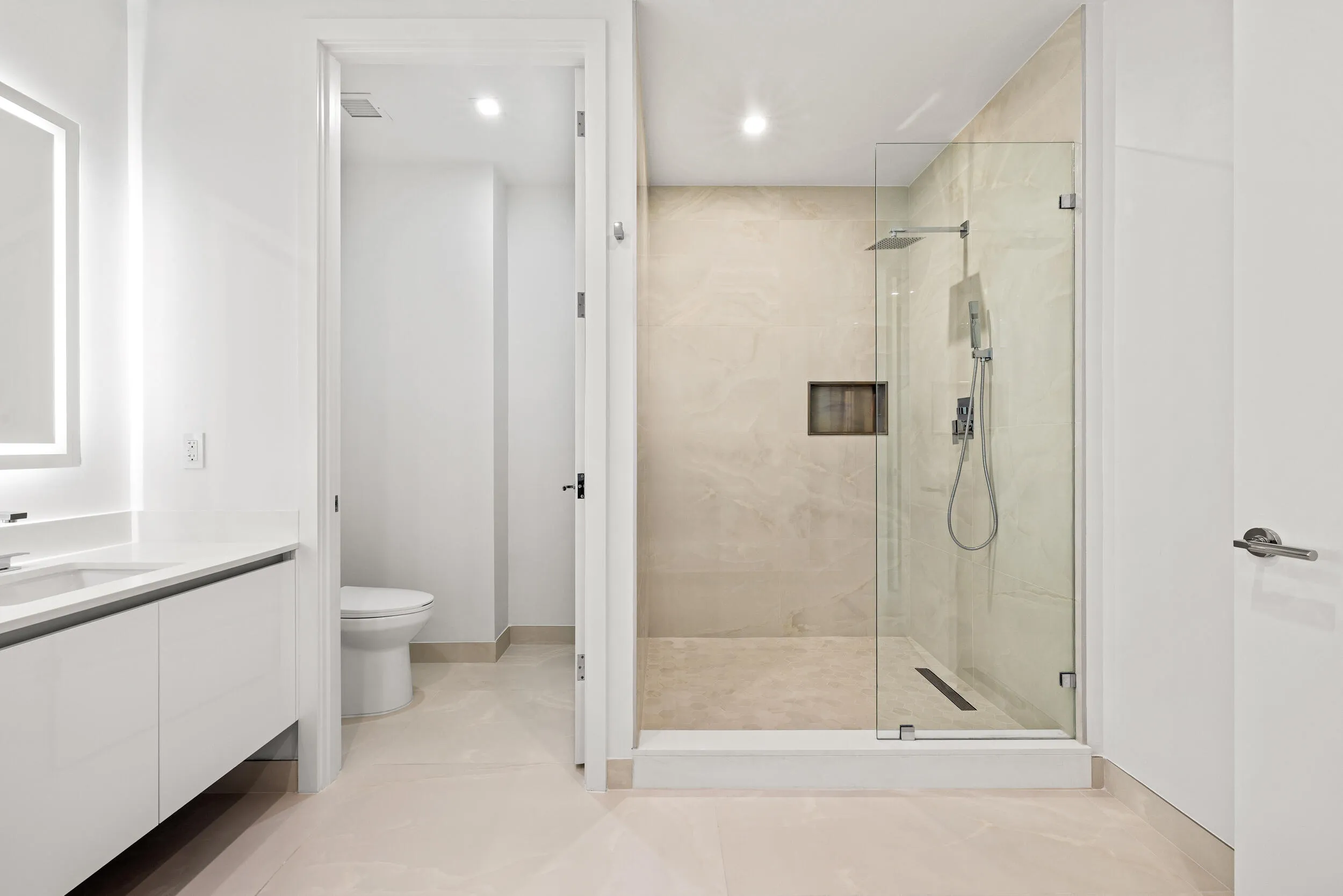 Master Bath - Modern bathroom featuring a frameless glass shower enclosure, a rainfall showerhead, and a vanity with an illuminated mirror