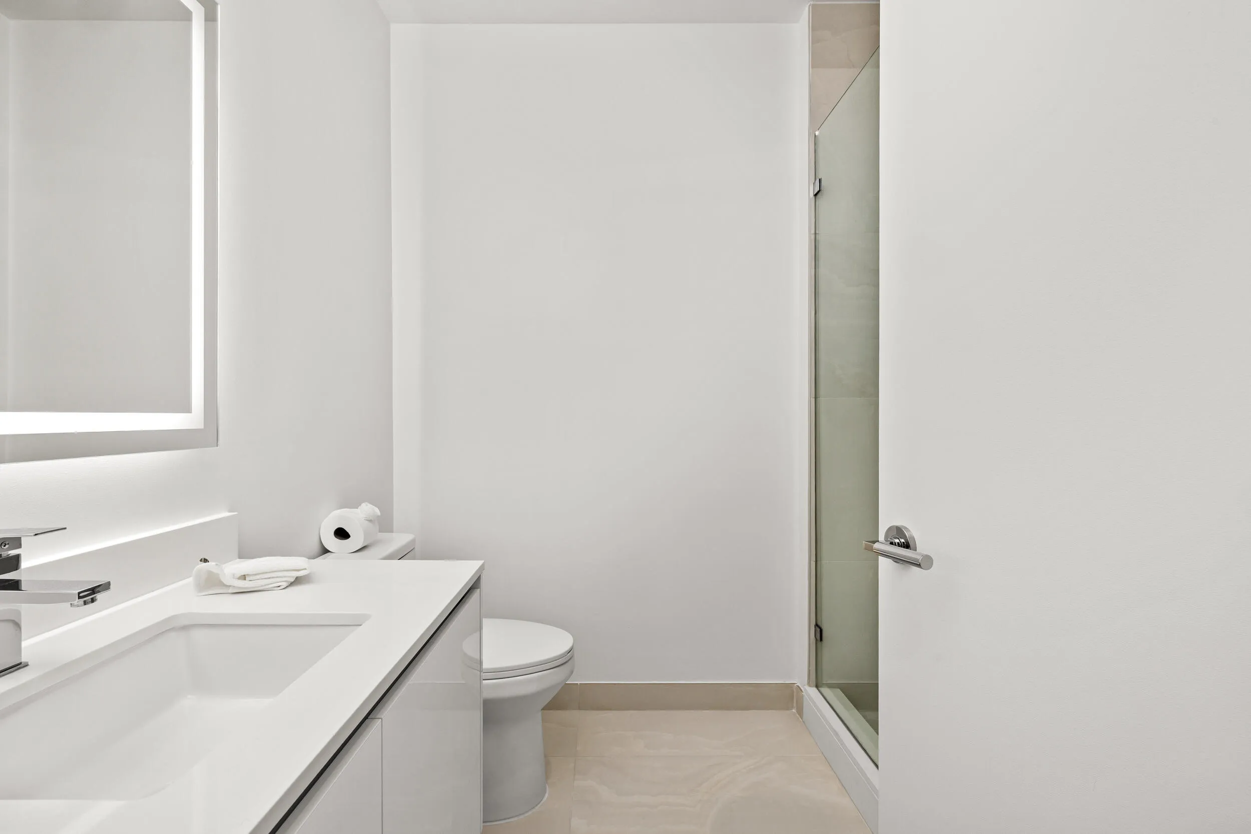 Modern vanity with integrated sink, chrome faucet, illuminated mirror, and glass-enclosed shower