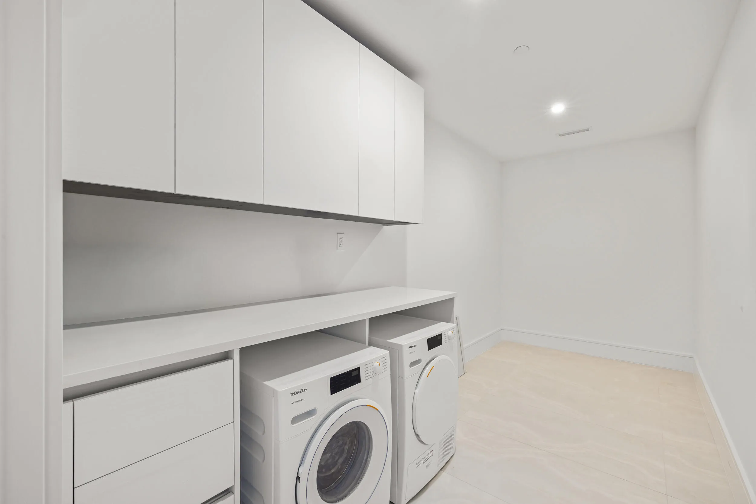 Integrated laundry appliances with extensive white cabinetry, a spacious countertop, and light-toned flooring