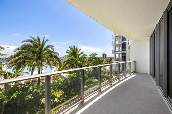 Expansive private balcony with glass railing, concrete flooring, and direct access to interior spaces through large glass doors