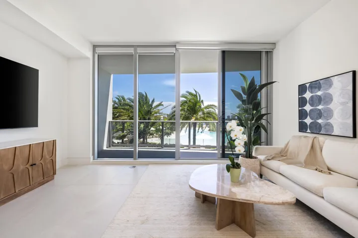 Expansive glass sliding doors open to a balcony with metal railings and tropical landscaping