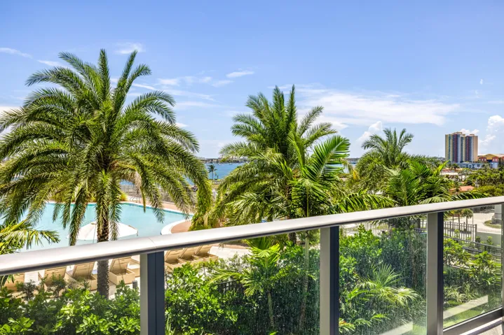 Glass balcony railing with aluminum supports, offering expansive views of tropical landscaping, a resort-style pool, and distant waterways