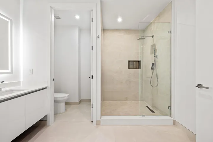 Master Bath - Modern bathroom featuring a frameless glass shower enclosure, a rainfall showerhead, and a vanity with an illuminated mirror