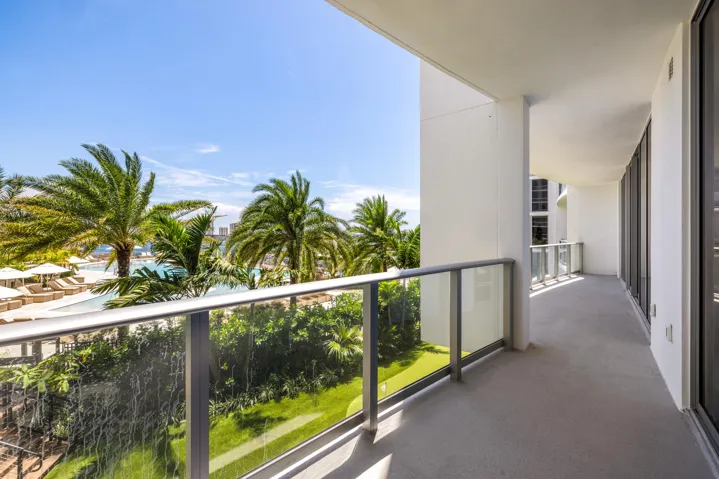 Expansive balcony with concrete flooring, glass panel railing, and large sliding glass doors