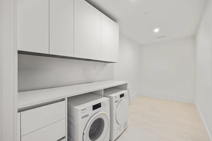Integrated laundry appliances with extensive white cabinetry, a spacious countertop, and light-toned flooring