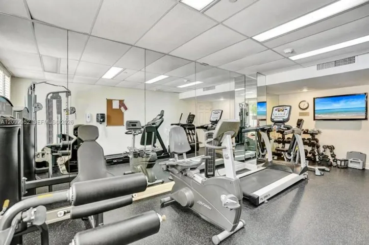 Fitness center featuring rubber flooring, drop ceiling with recessed lighting, and wall-to-wall mirrors