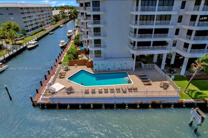 Waterfront swimming pool with a paved deck, perimeter fencing, and concrete bulkhead situated along a canal