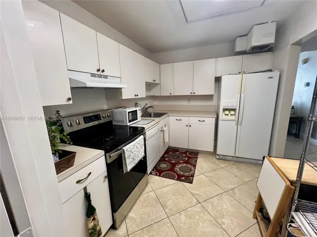 Kitchen featuring white cabinetry, solid-surface countertops, stainless steel appliances, and tile flooring