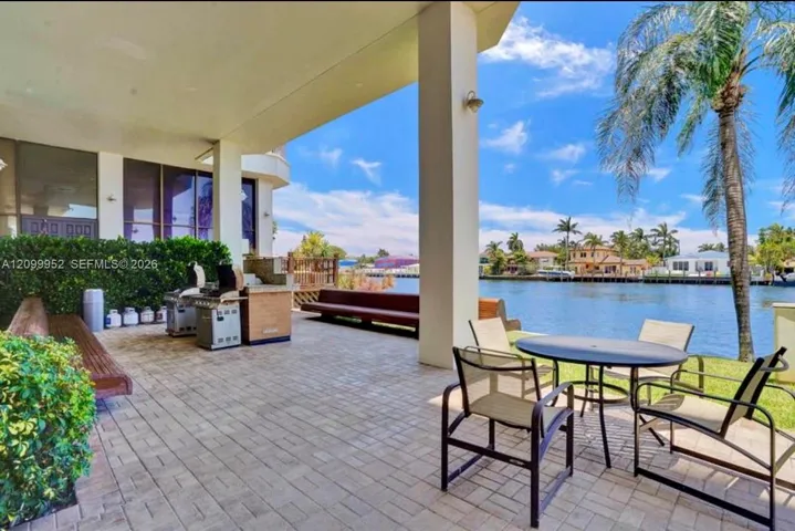 Covered outdoor patio featuring paver flooring, built-in stainless steel grill station, and water frontage