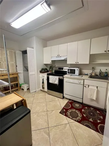 Kitchen featuring tile flooring, white cabinetry, integrated range hood, stainless steel appliance suite, and dedicated laundry closet with louvered doors