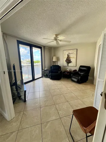 Large-format ceramic tile flooring, ceiling fan with integrated lighting, and full-height sliding glass doors opening to an exterior balcony