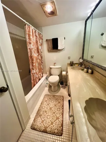 Full bathroom featuring a single vanity with a solid-surface countertop and integrated basin, a combination tub and shower with tile surround, and tiled flooring