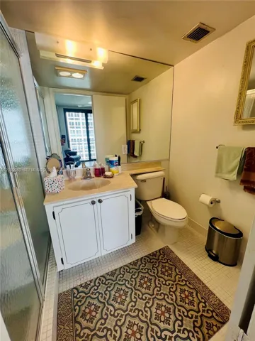 Bathroom featuring a vanity cabinet with white shaker-style doors, integrated sink, stone-finish countertop, full-width vanity mirror, and enclosed glass shower