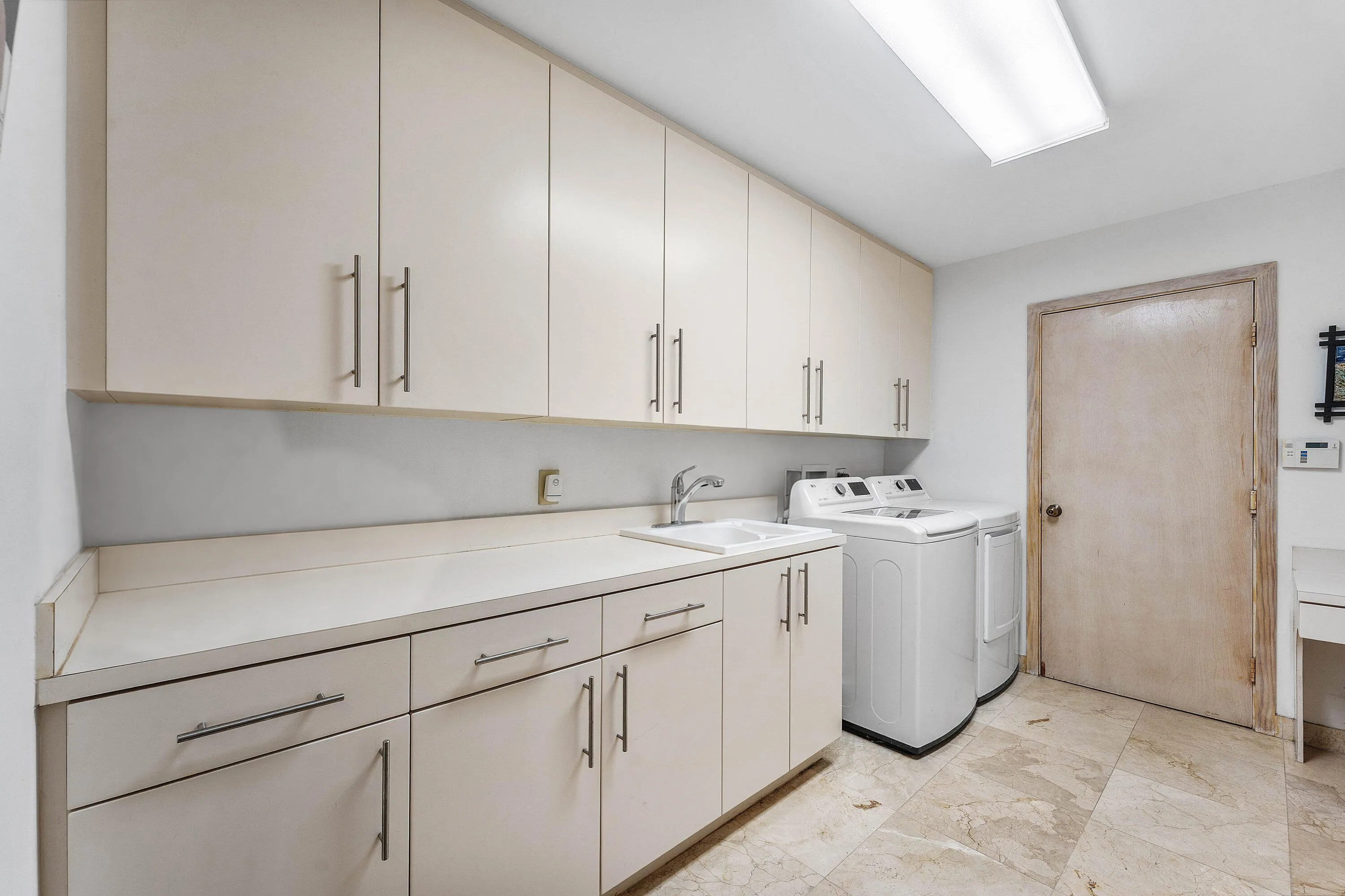 Laundry room featuring extensive upper and lower cabinetry, a built-in sink, solid surface countertops, and stone tile flooring