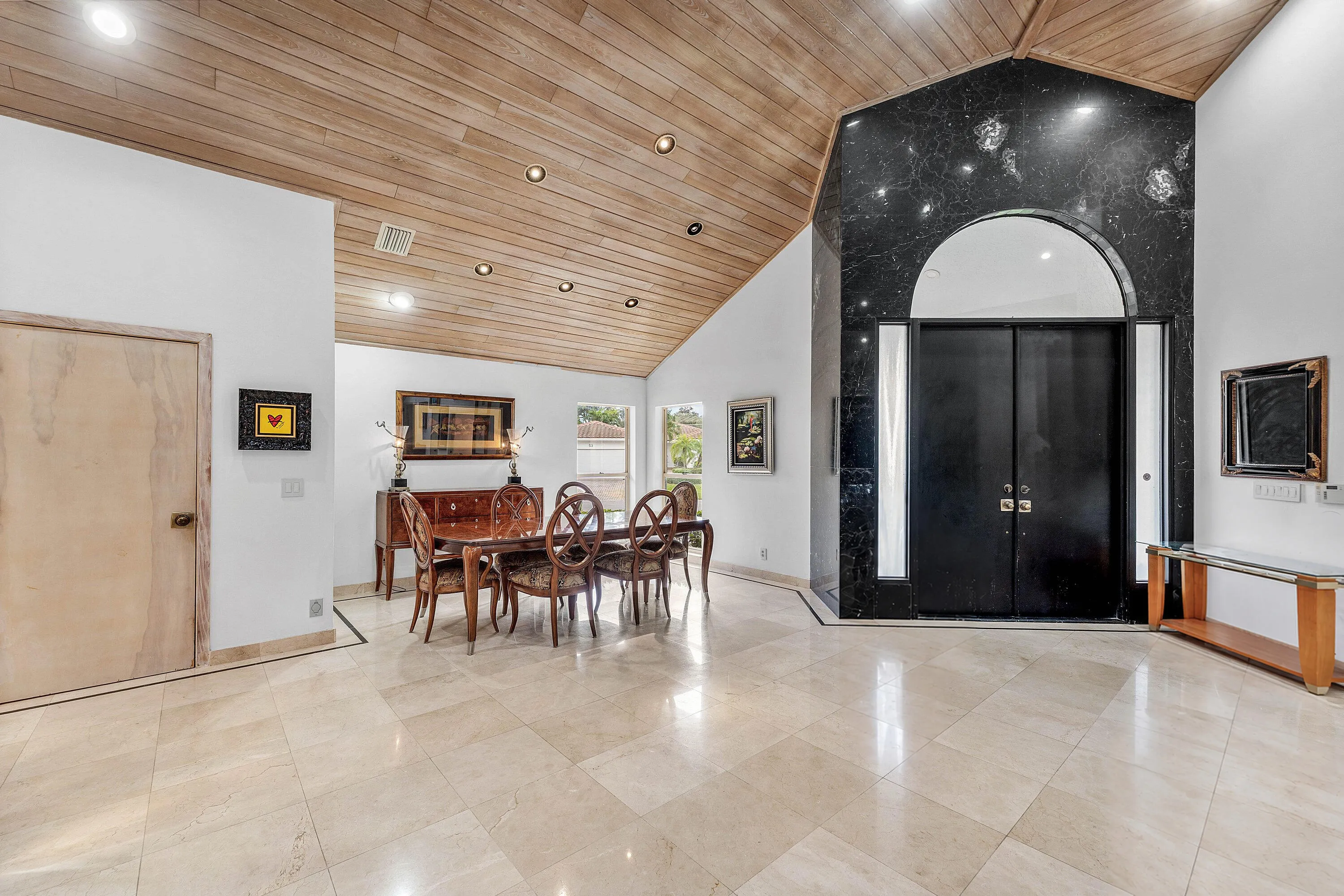 Vaulted wood-finish ceilings with recessed lighting, black double entry doors, a black stone accent wall, and polished tile flooring