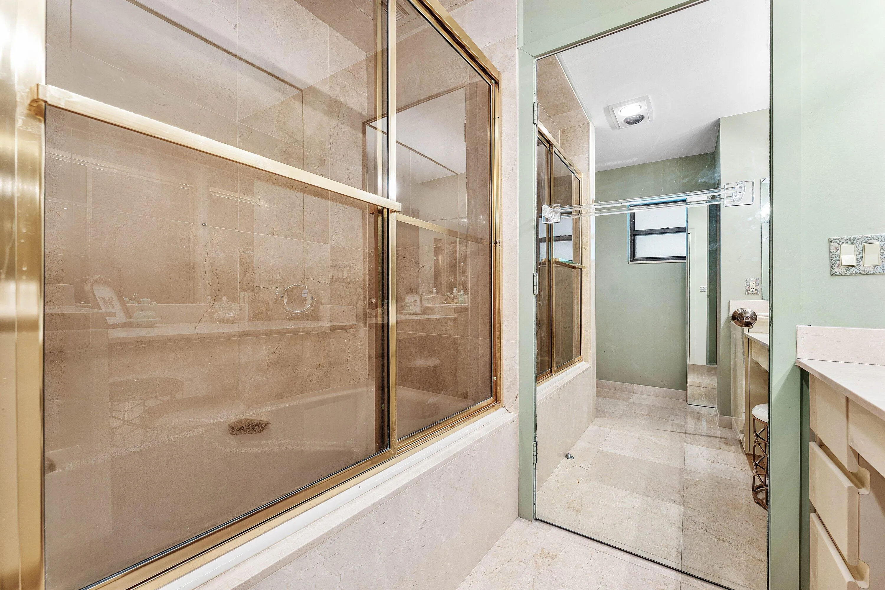 Full bathroom featuring a glass-enclosed shower with brass-toned framing, light-toned wall tile, and a built-in tub