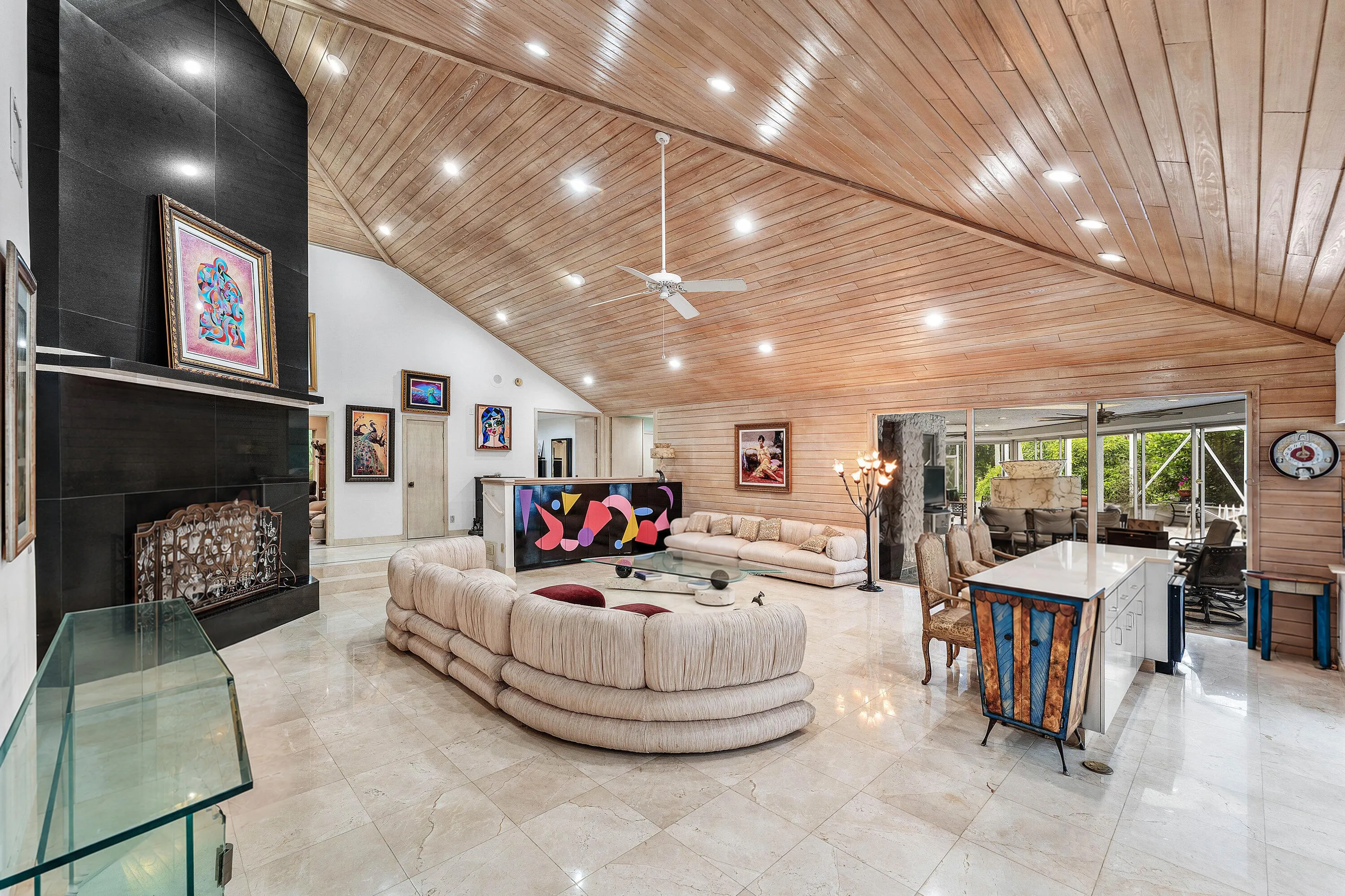 Vaulted wood-paneled ceiling with recessed lighting, large format tile flooring, black tile fireplace with mantel, and built-in white kitchen island with counter seating