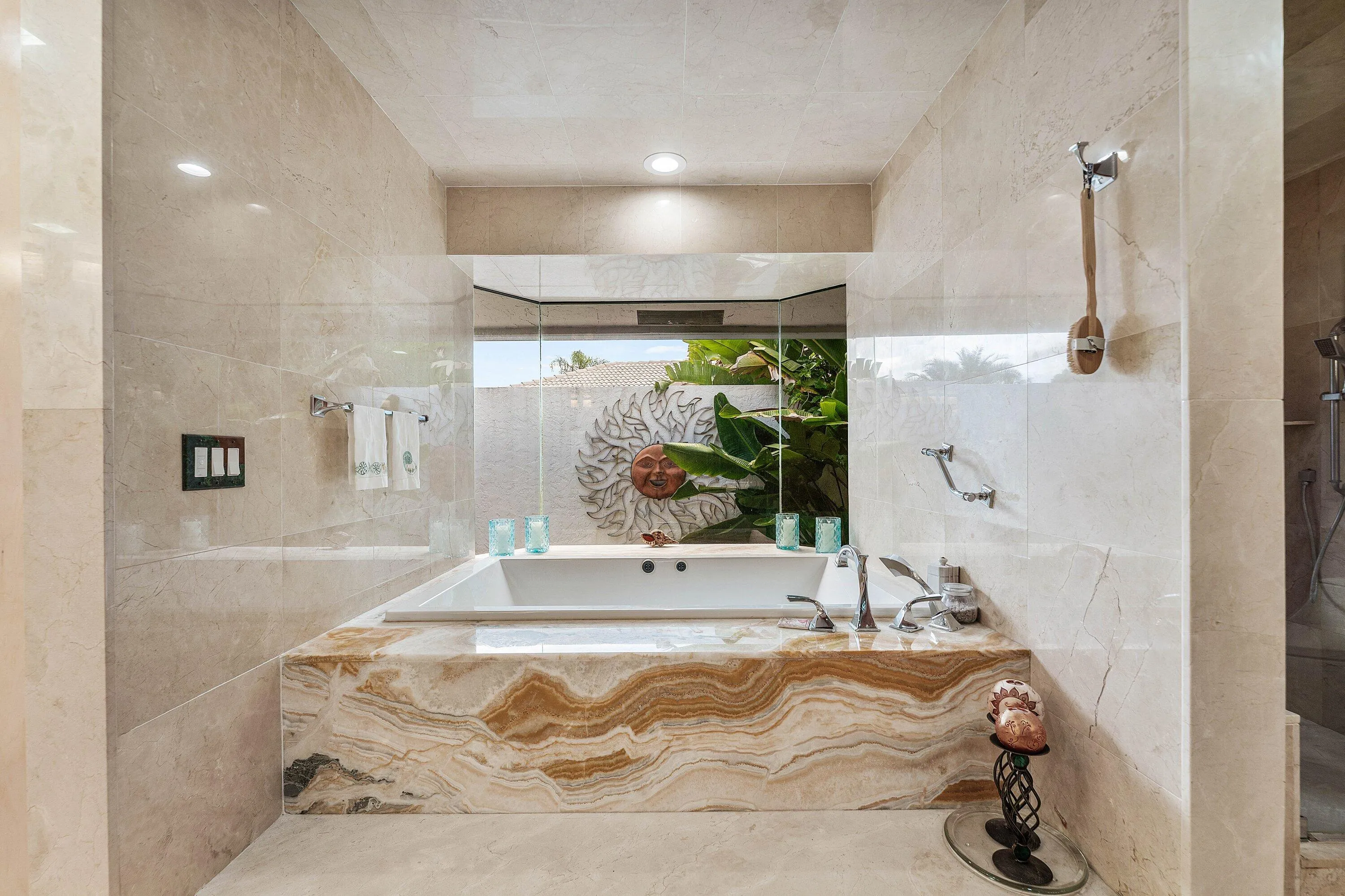 Built-in soaking tub with deck-mounted fixtures, surrounded by an onyx accent panel and light-toned tile walls