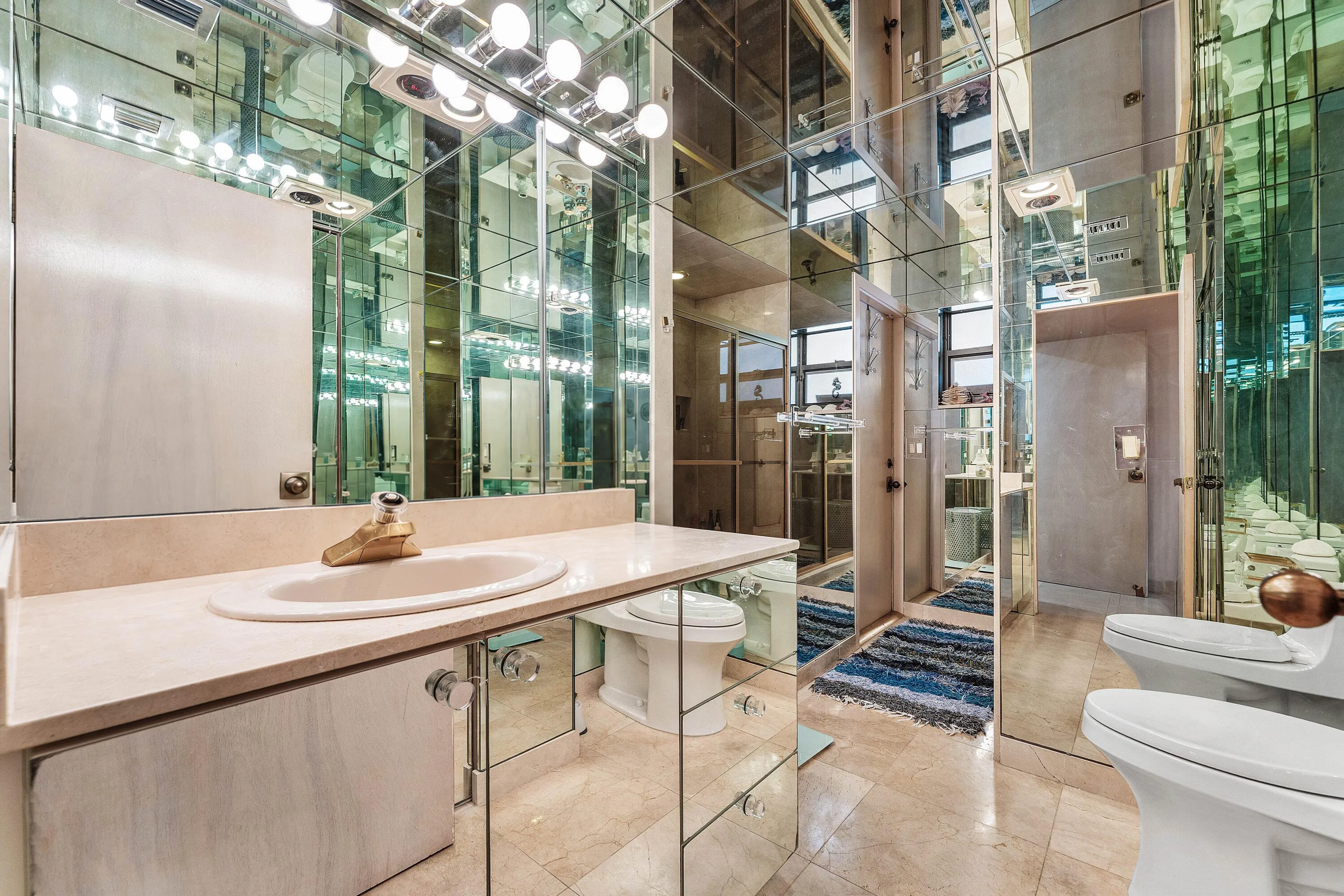 Mirrored wall finishes throughout, vanity with an integrated sink and light-toned countertop, vanity lighting fixture, and a toilet with an adjacent bidet