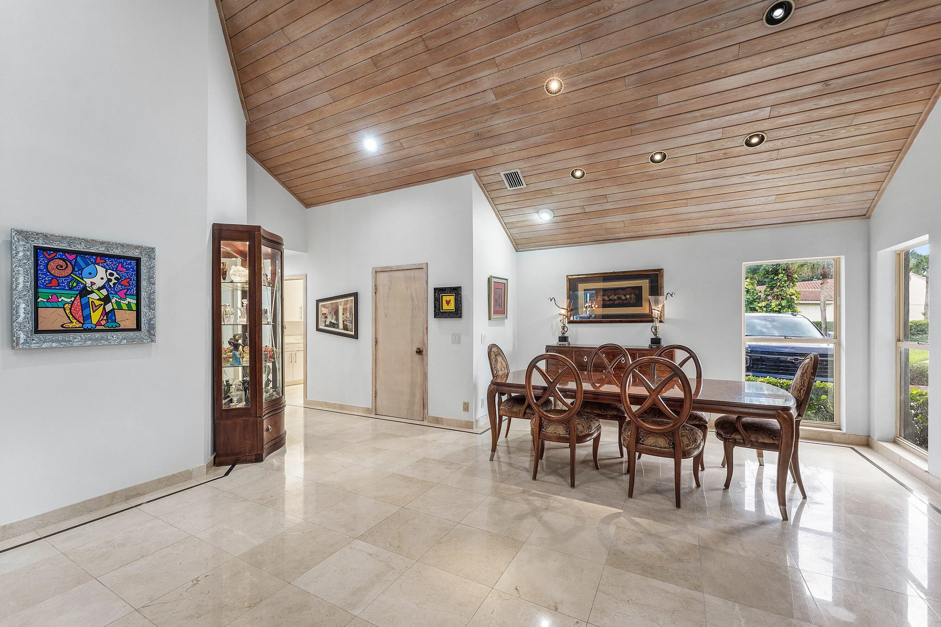 Vaulted wood-paneled ceiling with recessed lighting, light-toned stone tile flooring, and multiple windows providing natural illumination