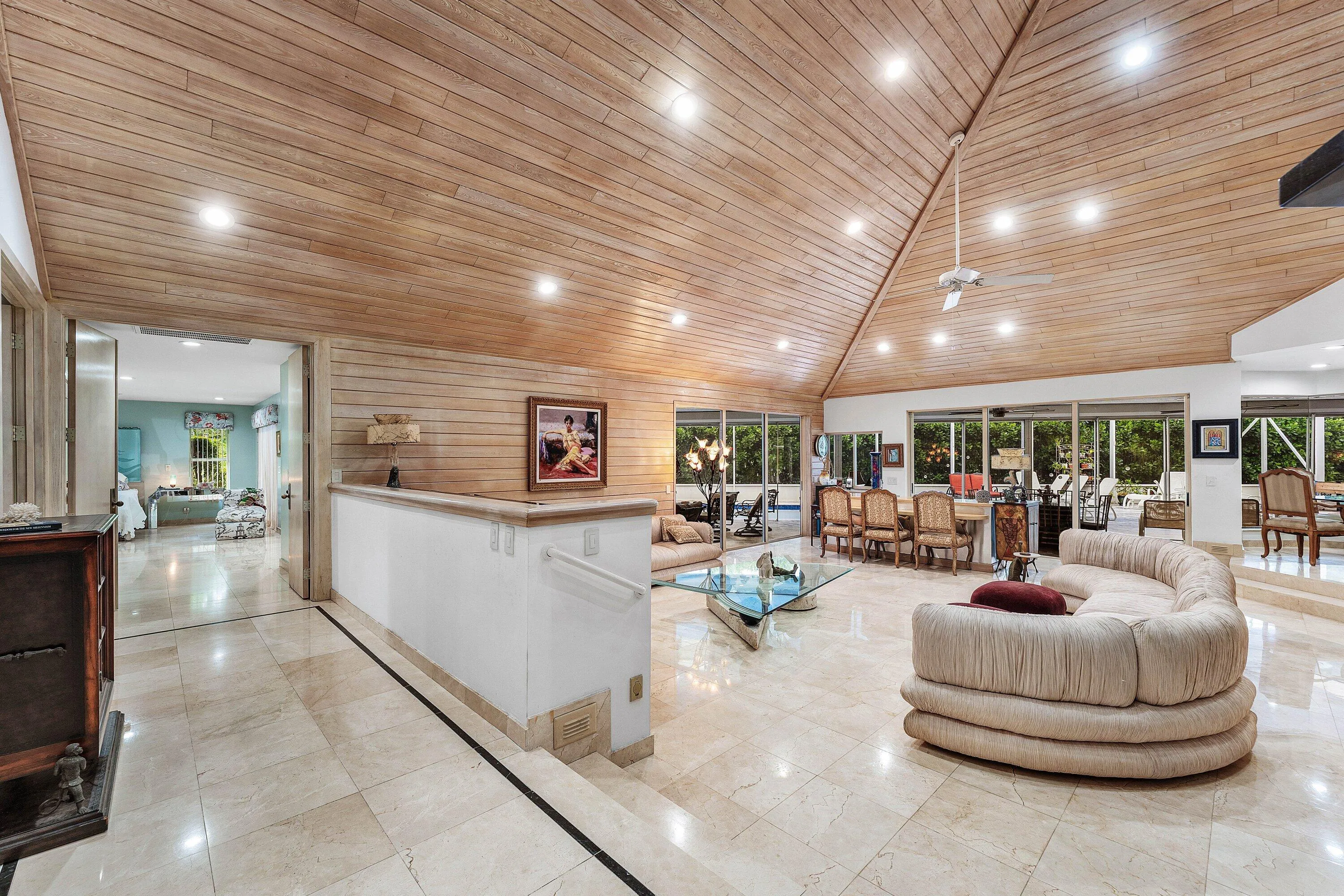 Vaulted wood-paneled ceiling with recessed lighting, stone tile flooring, half-wall with handrail, and expansive glass sliding doors