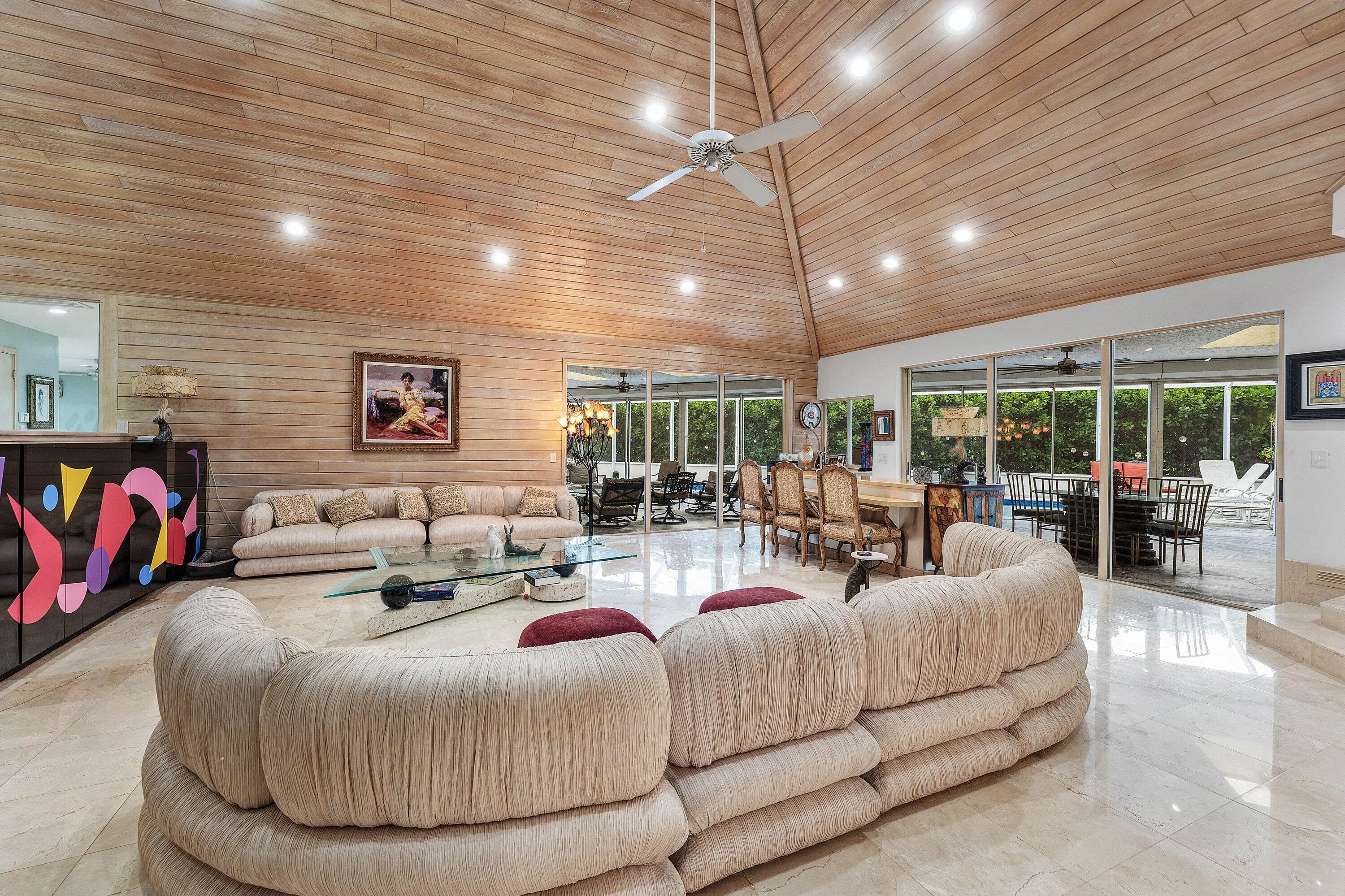 Vaulted wood-paneled ceiling with recessed lighting, large format tile flooring, and extensive glass sliding doors overlooking exterior