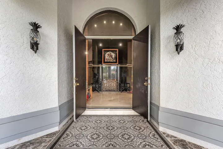 Arched entry with double doors, pineapple-motif sconces, and patterned inlay flooring