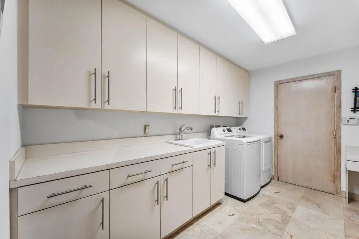 Laundry room featuring extensive upper and lower cabinetry, a built-in sink, solid surface countertops, and stone tile flooring