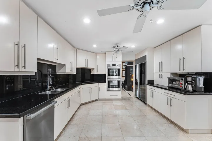 Expansive kitchen featuring abundant white cabinetry, black countertops, stainless steel appliances including double wall ovens, integrated wine cooler, and tile flooring