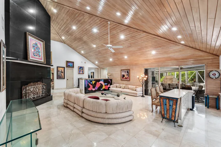 Vaulted wood-paneled ceiling with recessed lighting, large format tile flooring, black tile fireplace with mantel, and built-in white kitchen island with counter seating