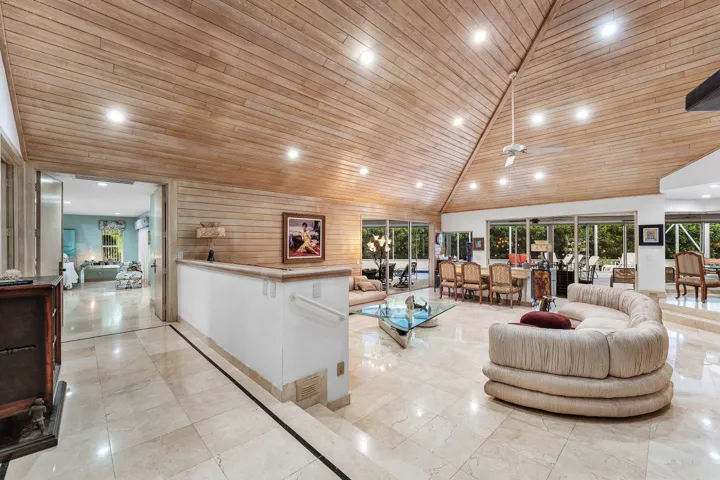 Vaulted wood-paneled ceiling with recessed lighting, stone tile flooring, half-wall with handrail, and expansive glass sliding doors