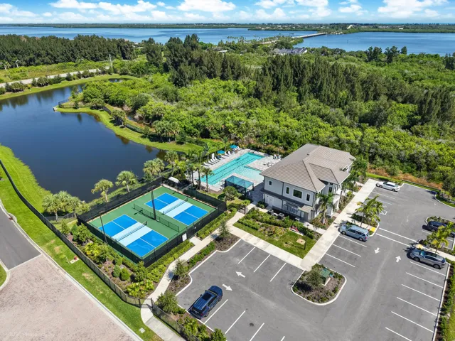Community building with a tiled roof, adjacent beach entry swimming pool, and pickleball courts