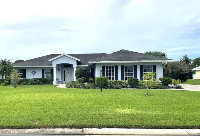 Exterior featuring a light blue facade, dark roof, prominent entryway with white columns, shuttered windows, and a landscaped front yard