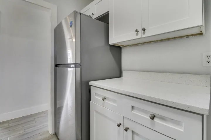 Stainless steel refrigerator, white shaker-style cabinetry, and light-toned countertops