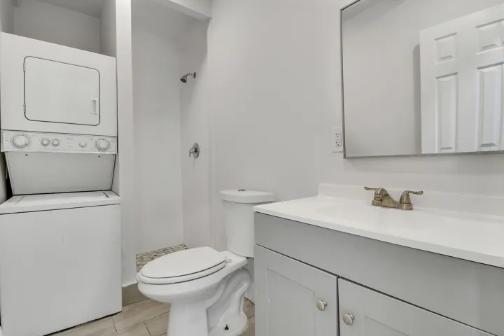 White stackable washer and dryer, light gray vanity with white countertop, chrome faucet, and rectangular mirror