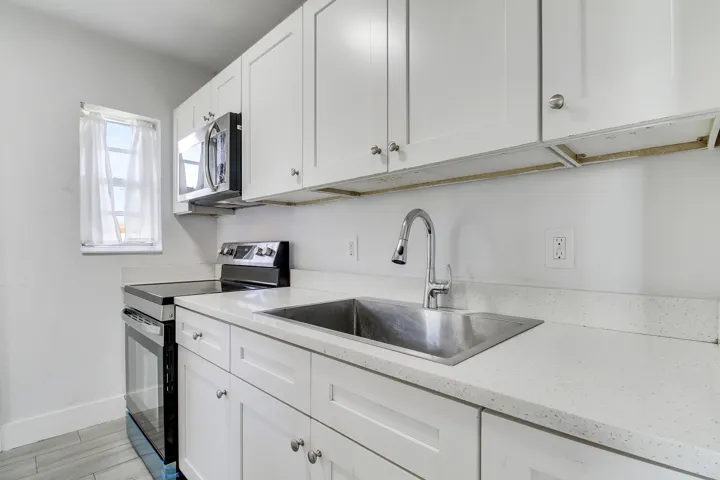 White shaker-style cabinetry with brushed nickel hardware, stainless steel undermount sink, contemporary gooseneck faucet, light-toned countertops, and tile flooring