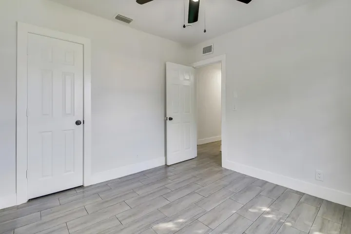 Neutral tone walls with light-colored tile flooring, white six-panel doors, and a ceiling fan with integrated lighting