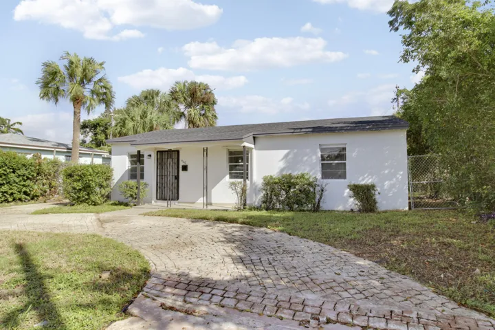 Single-story exterior with white stucco finish, dark shingle roof, and a paver driveway