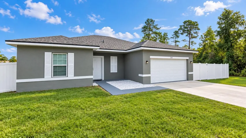 Gray stucco exterior with white trim and shutters, asphalt shingle roof, attached garage, and a concrete driveway