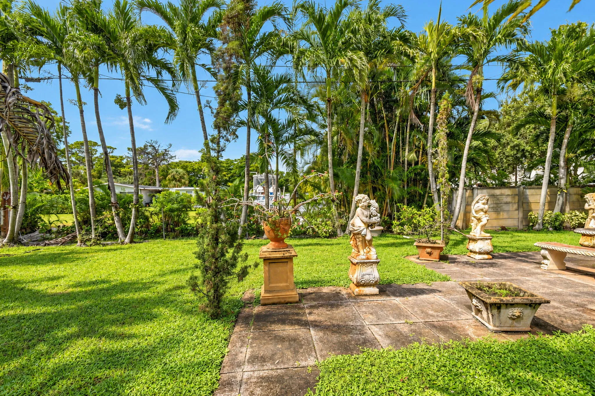 Manicured lawn with mature palm trees, flagstone patio, carved stone statuary, and built-in stone planter