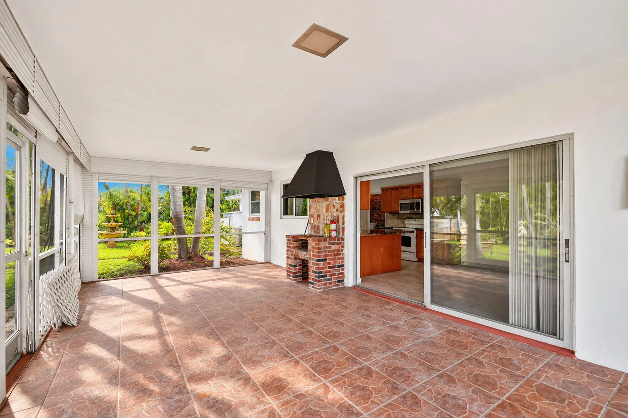 Screened enclosure with ceramic tile flooring, a built-in brick grilling station with an exhaust hood, and a sliding glass door entry to the interior