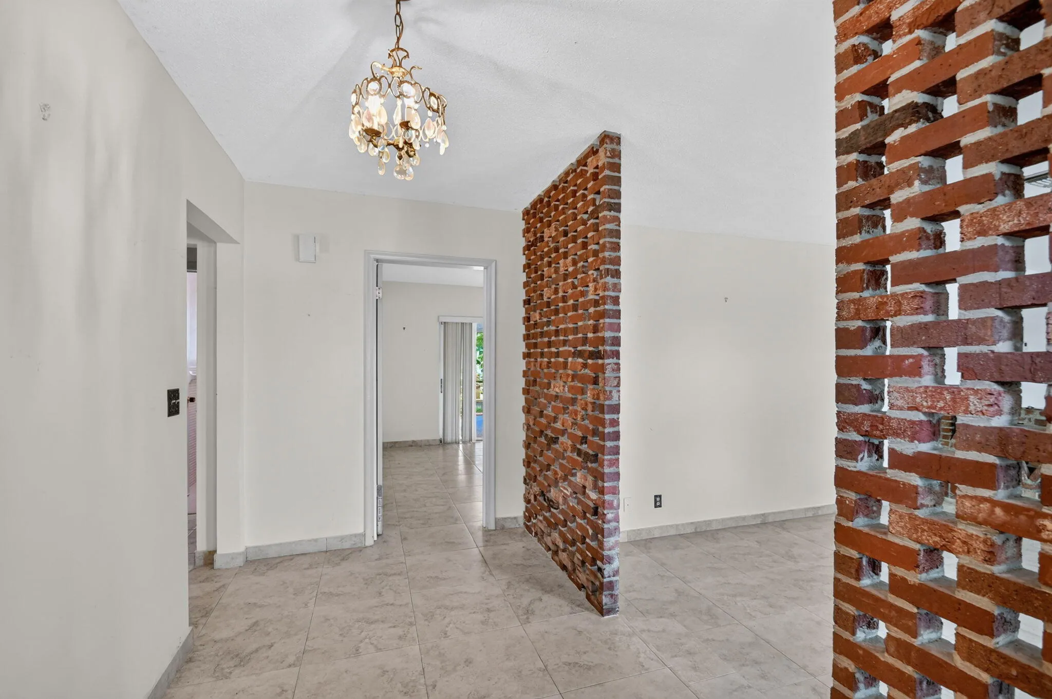 Brick screen wall, decorative chandelier, tile flooring, white walls, multiple doorways