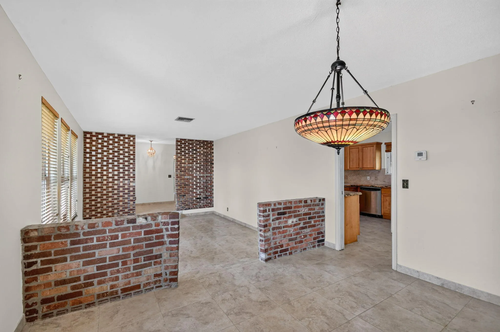 Tile flooring throughout with brick half-walls, a decorative ceiling light fixture, and a kitchen featuring wood cabinetry