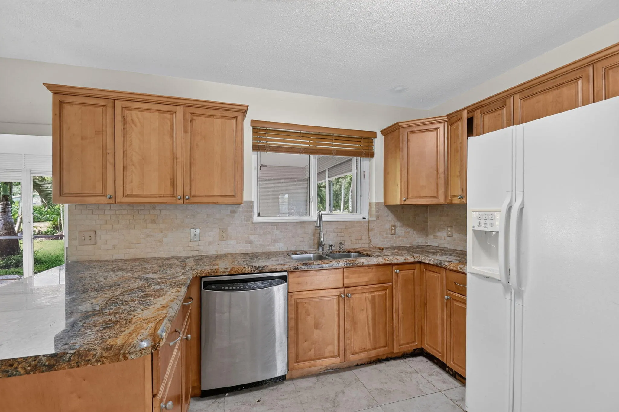 Wood-finish cabinetry with crown molding, stone countertops, stone tile backsplash, stainless steel dishwasher, and a window above the sink